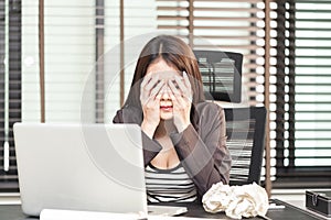 Tired young female executive sitting with crumpled paper balls a