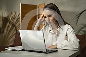 A tired young freelance woman uses a laptop, suffers from headaches, tension and migraines, and stress in the office. A