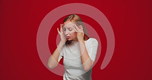 Tired young girl suffer migraine, long covid symptom. Sick female massaging temples suffering headache on red background