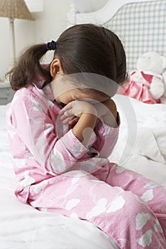 Tired Young Girl Wearing Pajamas Sitting On Bed