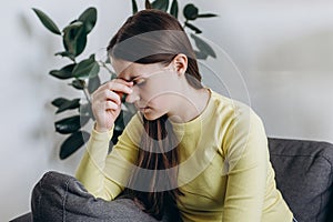 Tired young lady unwell stressed headache suffer depression sitting on sofa at home. Upset woman head pain ache discomfort