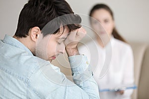 Tired young man having headache while working or visiting doctor