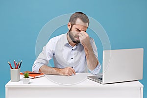 Tired young man in shirt sit work at desk with pc laptop isolated on pastel blue background. Achievement business career