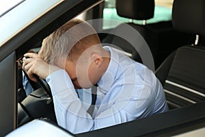 Tired young man sleeping on steering wheel in car