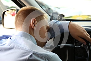 Tired young man sleeping on steering wheel in car