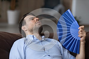 Tired young man wave with hand fan suffer from heatstroke