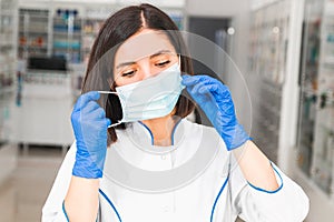 Tired young middle-east ethnicity doctor or pharmacist taking off blue medical mask and gloves in hallway of hospital