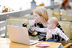 Tired young mother holding 6-month daughter and drinking coffee