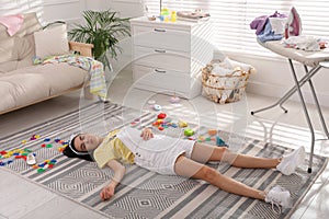 Tired young mother sleeping on floor in messy living room