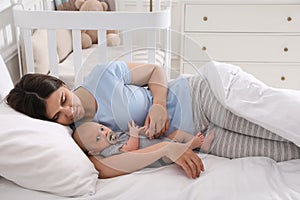 Tired young mother sleeping with her baby in bed