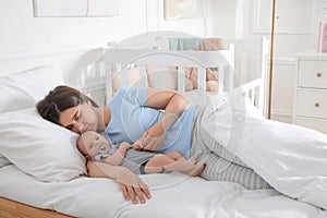 Tired young mother sleeping with her baby in bed at home