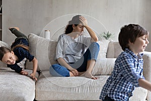 Tired young mother suffering from headache, exhausted by noisy kids