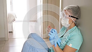 Tired young nurse in goggles and a medical mask is resting sitting on the floor.