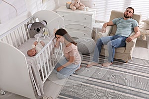 Tired young parents and their baby sleeping in children`s room