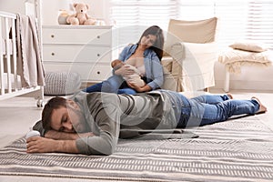 Tired young parents with their baby sleeping on floor in children`s room