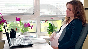 Tired young pregnant woman resting in her work place. Female caress tender belly