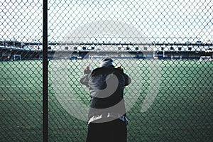 Tired young sporty man leaned and holding on to the rabitz fence