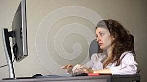 Tired young woman with curly hair and white shirt is working at the office using her computer, routine work, freelance