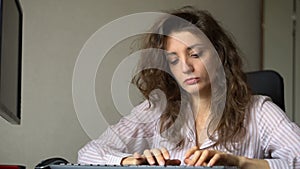 Tired young woman with curly hair and white shirt is working at the office using her laptop, routine work, freelance