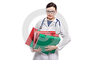 Tired young woman doctor with stethoscope holding binders in her hands in white uniform on white background