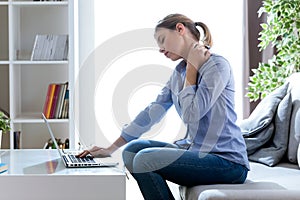 Tired young woman with neck pain using her laptop at home.