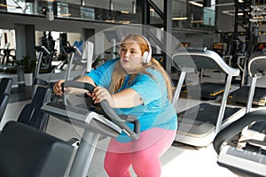 Tired young woman with obesity on treadmill during training workout