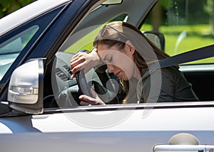 Tired young woman sitting in car leaning on steerin wheel with eyes closed