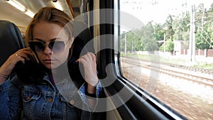 A tired young woman in sunglasses with a travel neck pillow sleeps on the train.