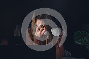 Tired young woman working behind a laptop at night, sick eyes.