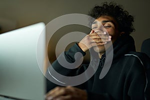 Tiredness. Sleepy young guy holding hand over his mouth while yawning. Male student studying using laptop, sitting in