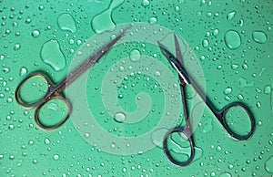 Titanium manicure scissors for trimming cuticles. Water drops green background.