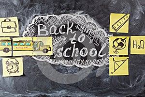 Title Back to school written by chalk on the black chalkboard and the school bus drawn on the pieces of paper