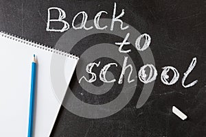 Title Back to school written by white chalk and the the notebook with blue pencil on the black school chalkboard