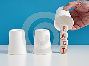 To discover the hidden facts concept. Man playing the shell game with three cups reveals the word risk on wooden cubes