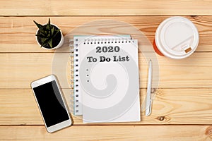 To do list Concept - 2020 number and text on notepad. Modern workspace with smartphone, paper, notebook and female hands on wooden