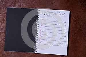 To-do list for a week. Open notebook with black cover on brown background photo