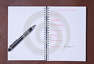 To-do list for a week. Open notebook with black cover on brown background photo