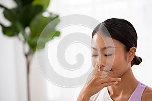 To guide her breath, an Asian lady touches her nostrils with her fingers. To get started with yoga and meditation