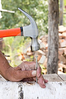 To hammer a nail with a hammer. Older worker carpenter