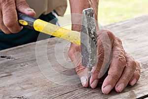 To hammer a nail with a hammer. Older worker carpenter