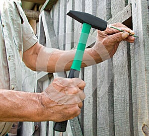 To hammer a nail with a hammer. Older worker carpenter