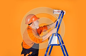 To make repairs. man in working clothes painting wall in empty room. painter in overall and cap with paint bucket