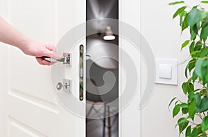 To open the door. Modern white door with chrome metal handle and a man`s arm
