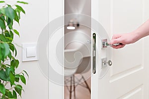 To open the door. Modern white door with chrome metal handle and a man`s arm