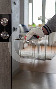 To repair an interior door  a master repairs a door with a screwdriver  a man with a screwdriver in his hand.