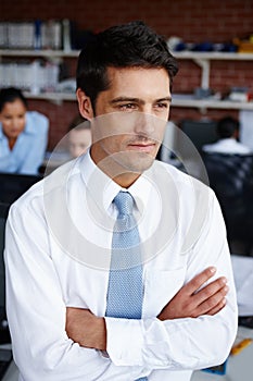 To succeed you need to be inspired. A handsome young businessman crossing his arms and looking away thoughtfully.