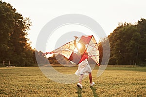 To the sunset. Happy girl in white clothes have fun with kite in the field. Beautiful nature