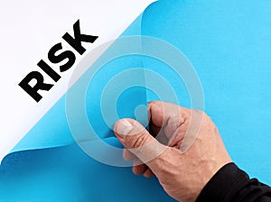 To uncover hidden business risks concept. Male hand opens the blue paper and reveals the word risk