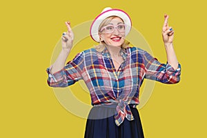 With to win. Portrait of hopeful pleased modern stylish mature woman in casual style with hat and eyeglasses standing with crossed