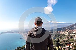 Toarmina - Tourist man with panoramic view on snow capped Mount Etna and the Mediterranean sea from Taormina, Sicily, Italy